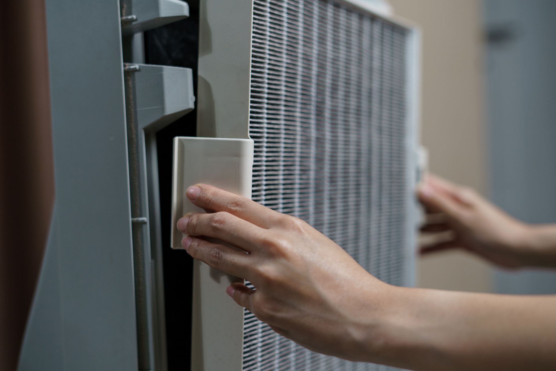 Hands holding the frame of a white air purifier filter while inserting it into the device.