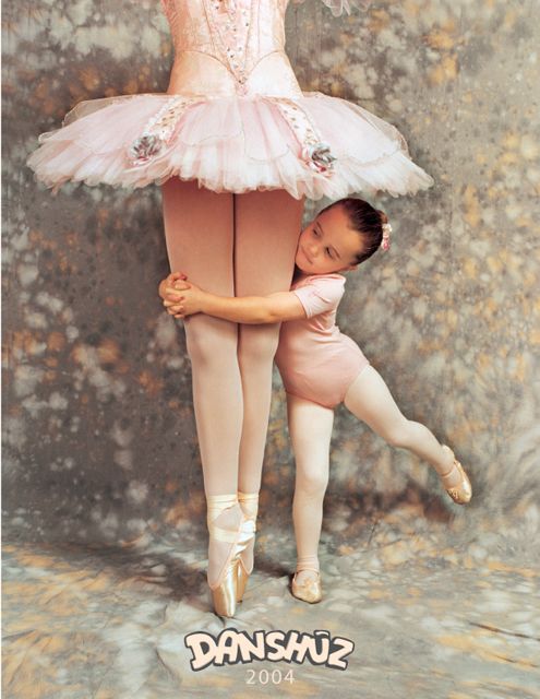 A small child in pink dancewear hugs the legs of a ballerina wearing a pale pink tutu and pointe shoes.