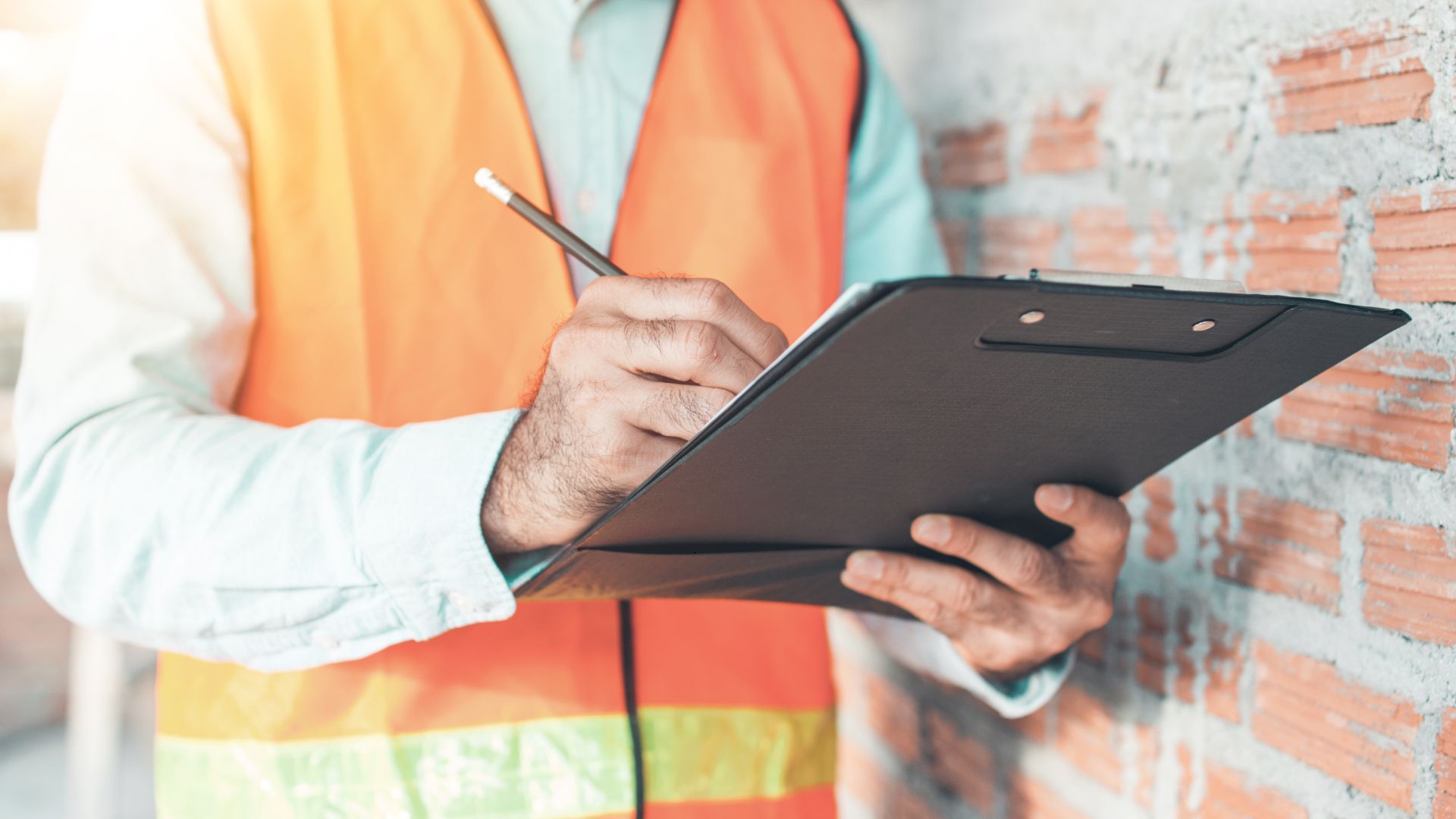 A construction worker is holding a clipboard and writing on it.