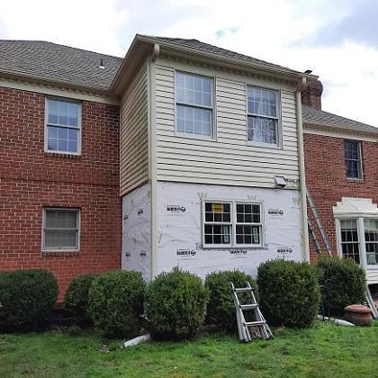 A brick house with a white siding and a ladder in front of it.