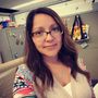 A woman wearing glasses is taking a selfie in a cubicle
