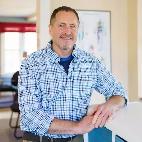 A man in a plaid shirt is leaning on a counter and smiling.