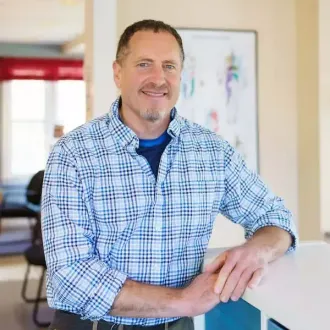 A man in a plaid shirt is leaning on a counter and smiling.