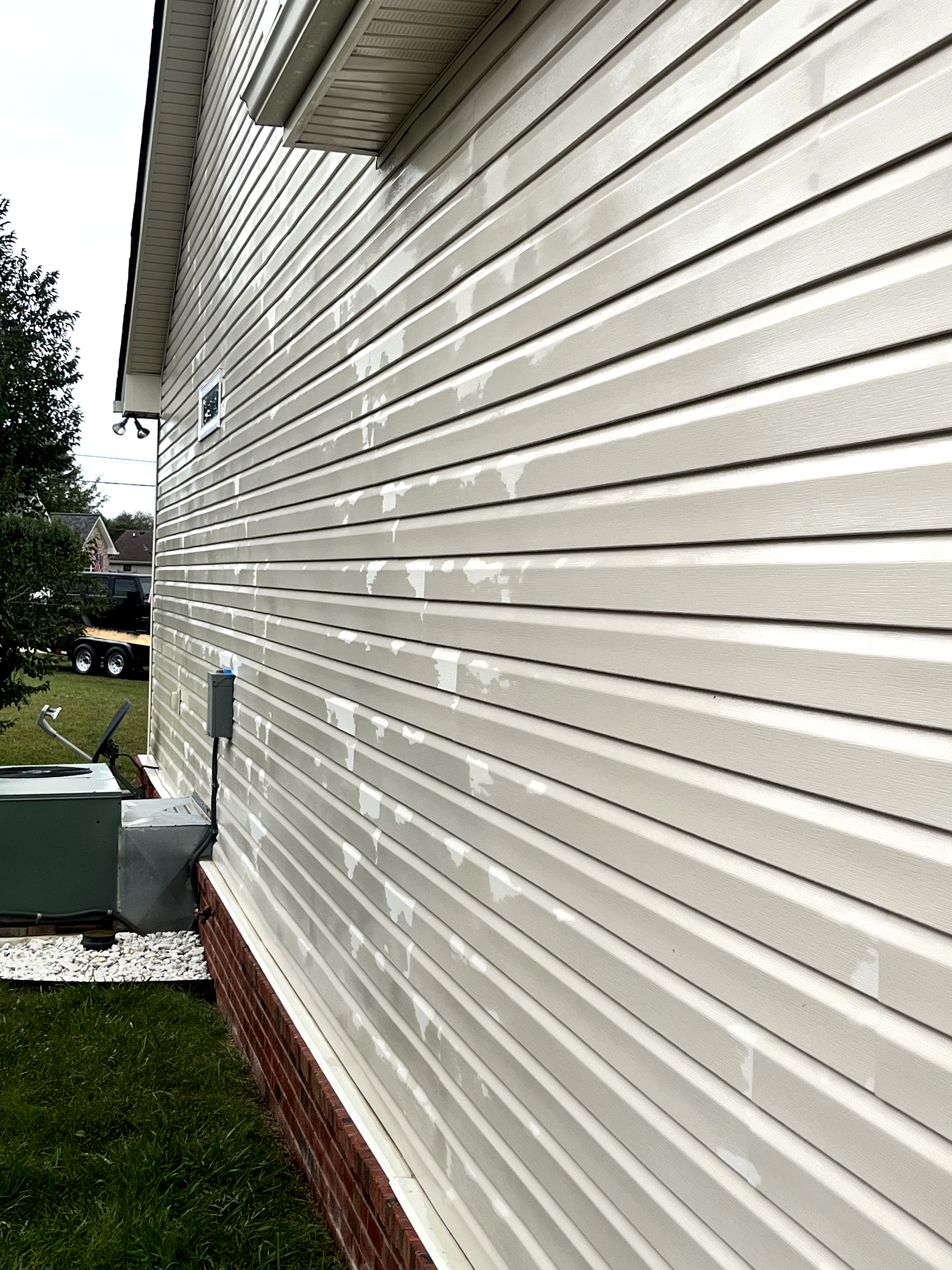 The side of a house with white siding and a brick foundation.