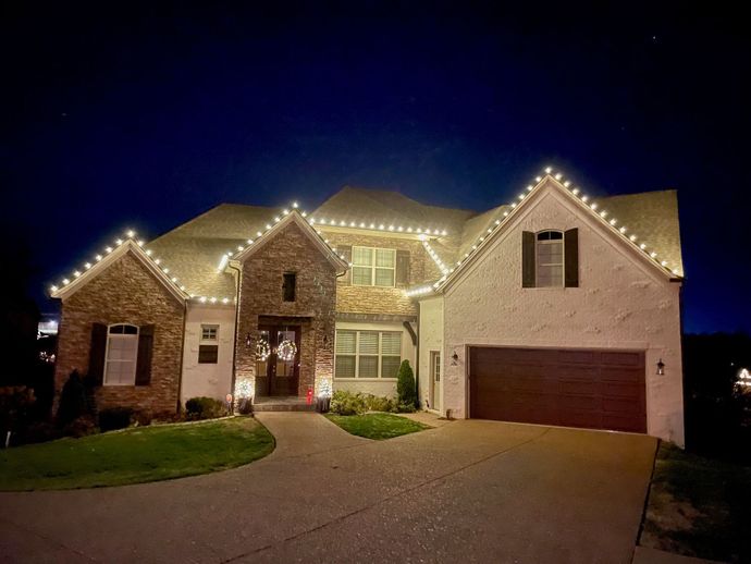 A large house with christmas lights on the roof is lit up at night.