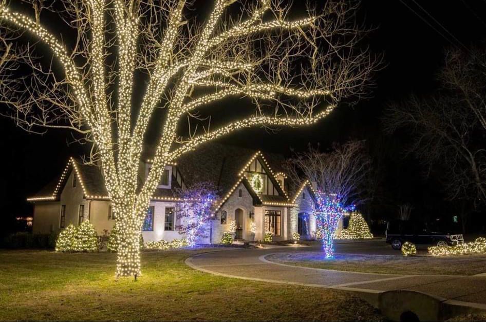 A house is decorated with christmas lights and a tree is lit up at night.