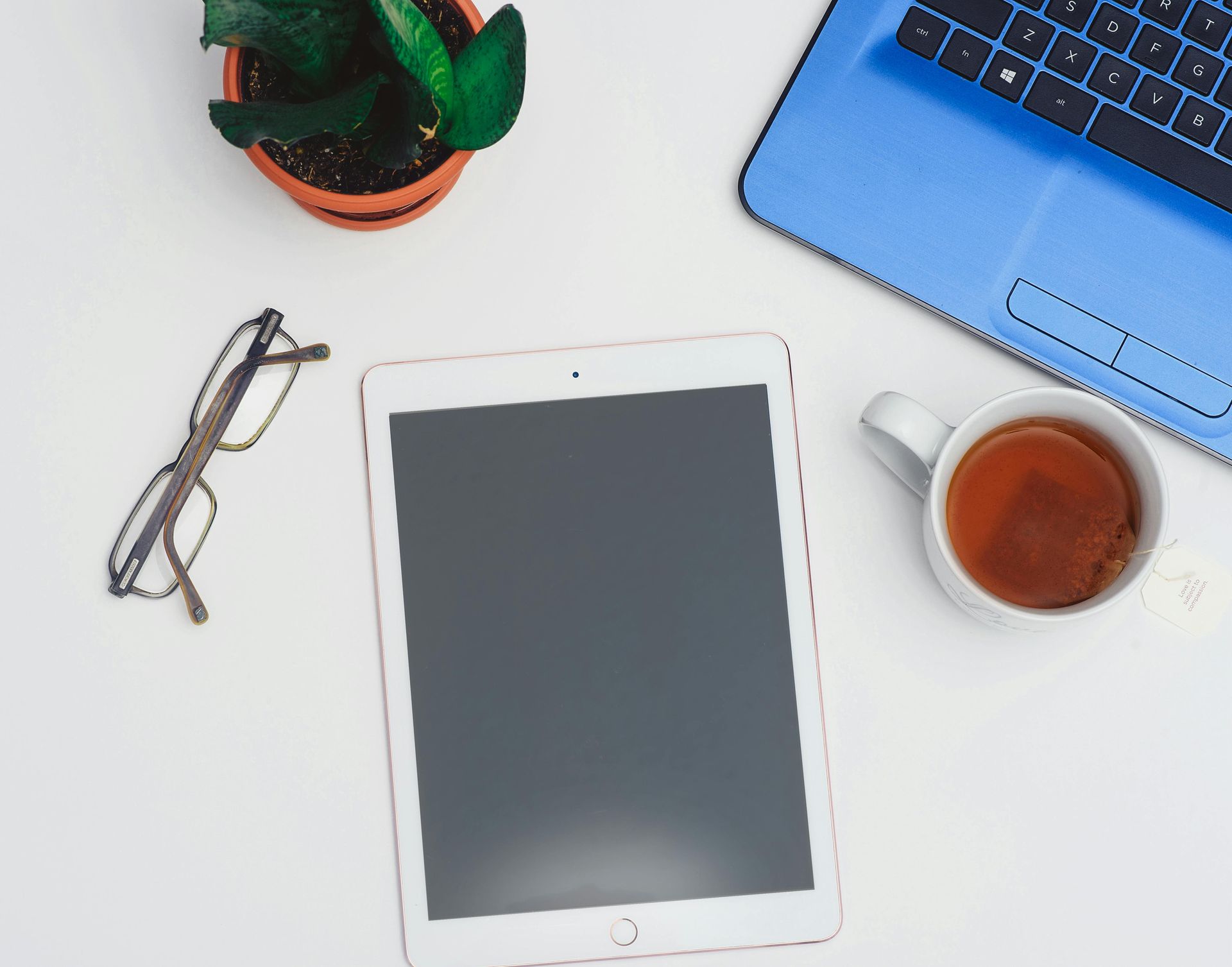 From left to right: eye glasses, tablet, tea cup filled with tea, laptop