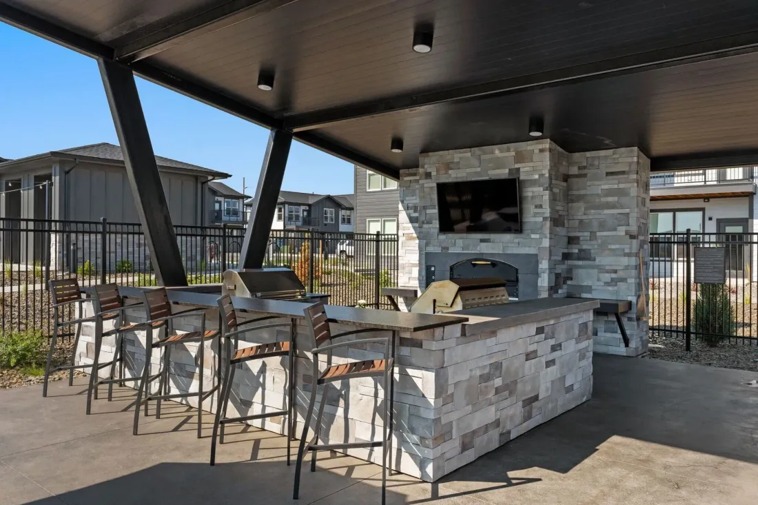 Outdoor covered patio with stone grill, bar seating, and tables under a modern roof.