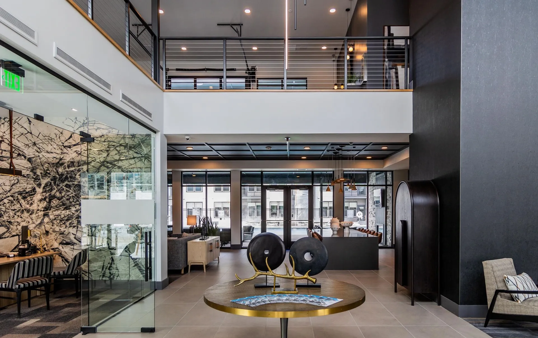 Modern office lobby with glass walls, a mezzanine, and a central round table sculpture.