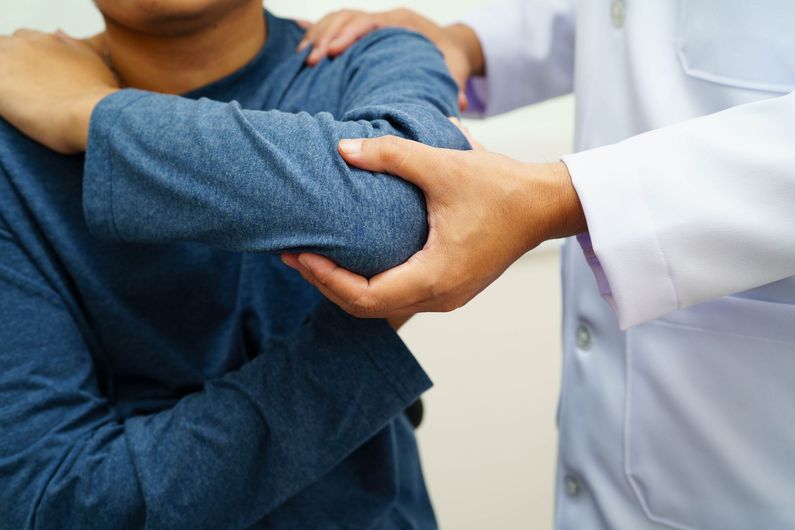 Doctor examining a patient’s arm in a clinic, with the patient wearing a blue shirt