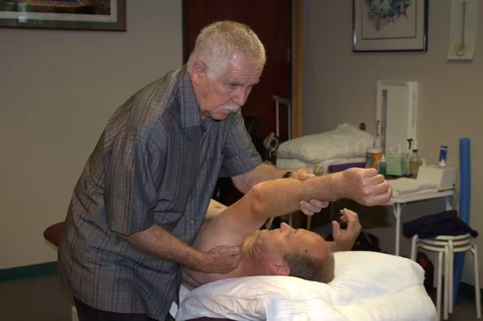 Physical therapist assisting a patient with arm stretching on a treatment table in a clinic room