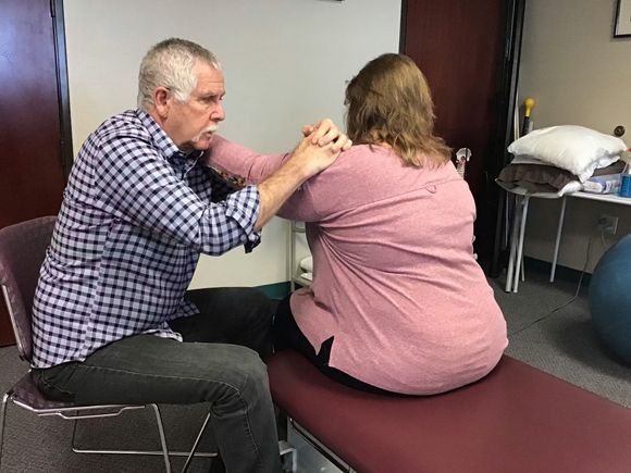 Therapist guiding seated patient through shoulder exercises in a treatment room