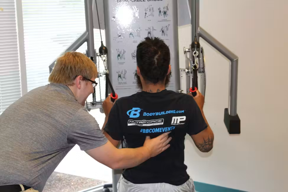 Trainer assisting person using a cable machine in a gym