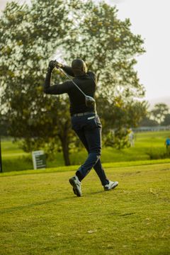 Golfer mid-swing on a grassy course with trees in the background