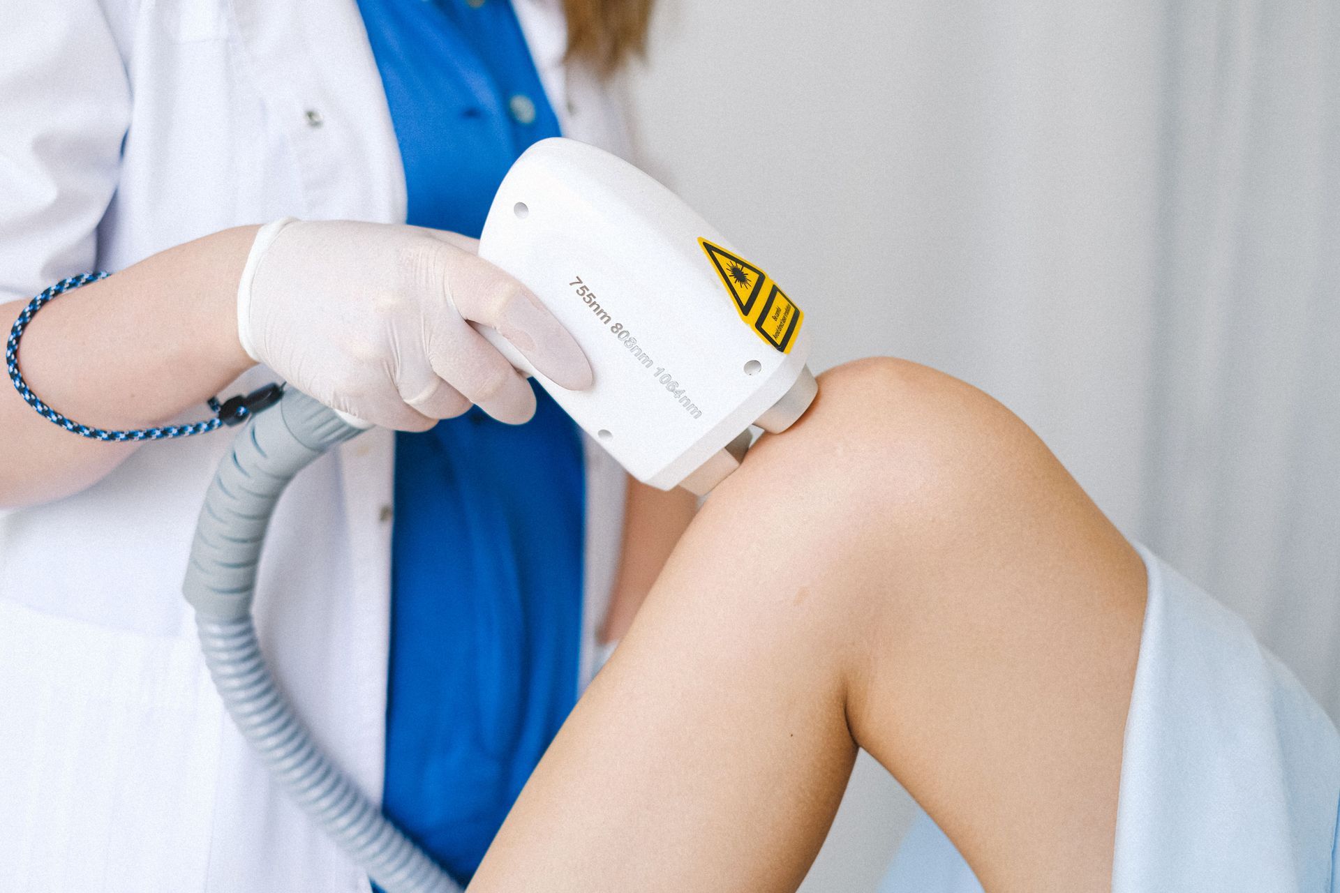 Gloved clinician using a laser device on a patient’s leg in a medical treatment room