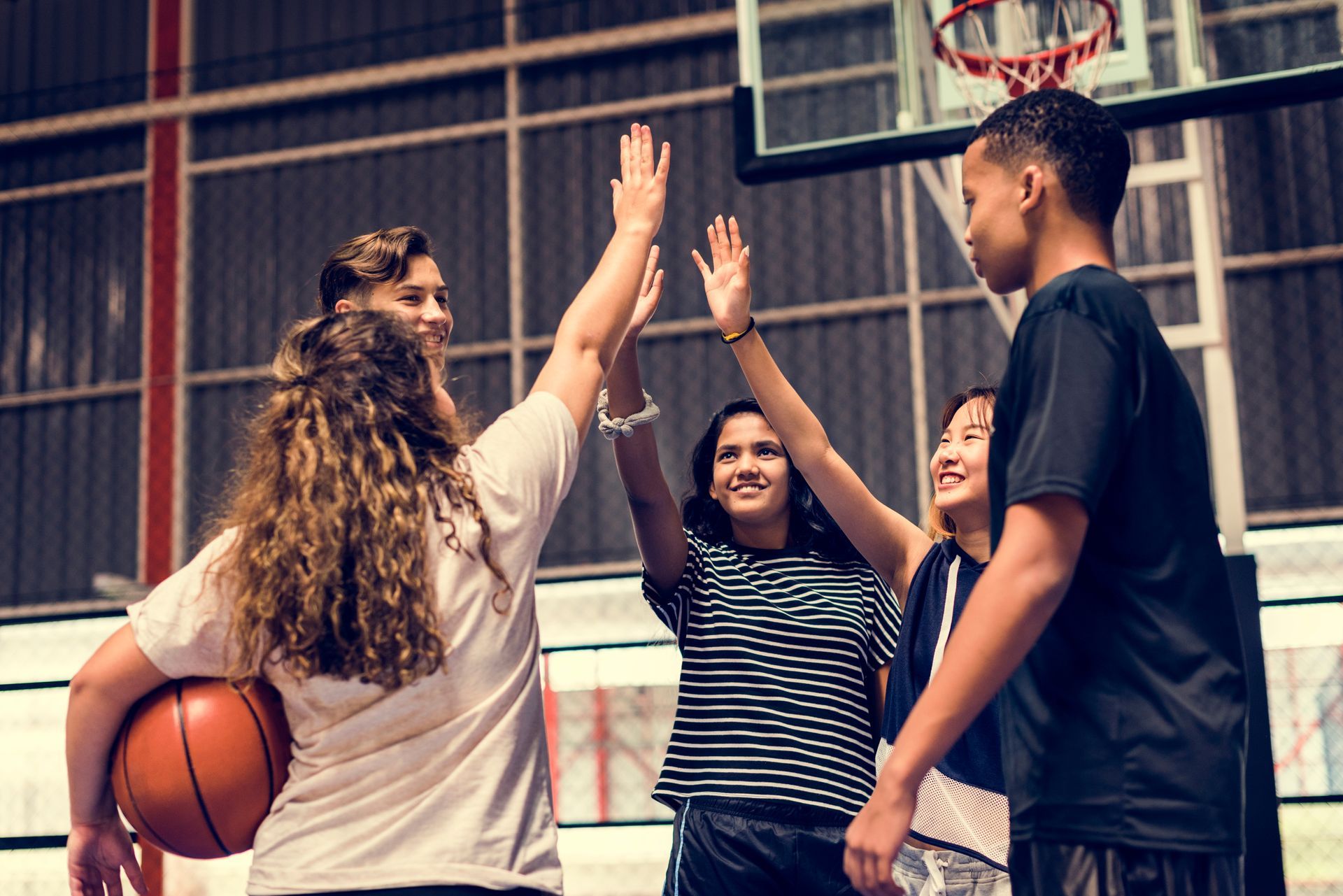 Three people high-five on an indoor basketball court, with one holding a basketball.