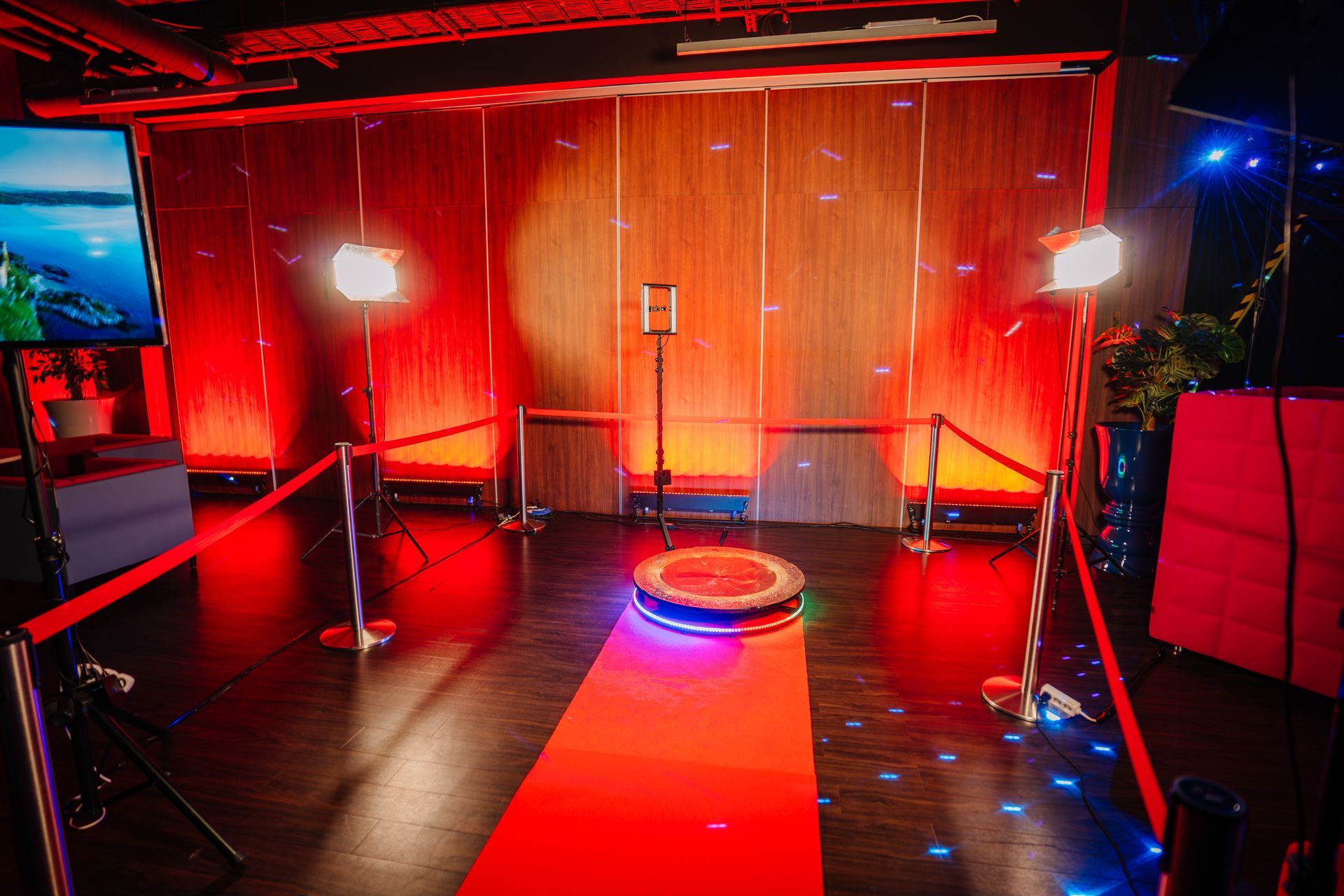 Red-lit photo booth setup with a circular platform and ropes. Two spotlights illuminate the space.