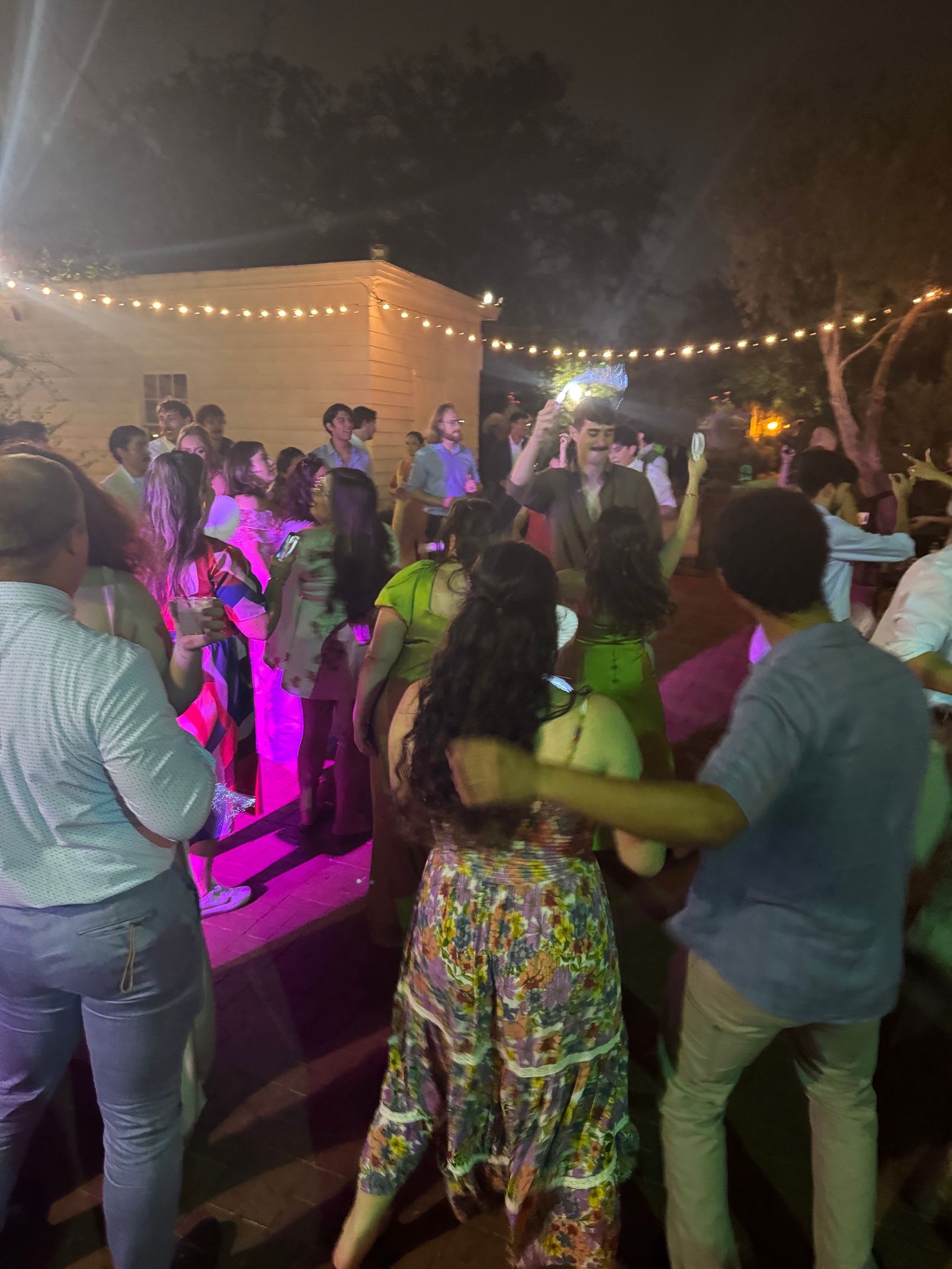 People silhouetted in a club with colorful light flares and pink/red lighting.