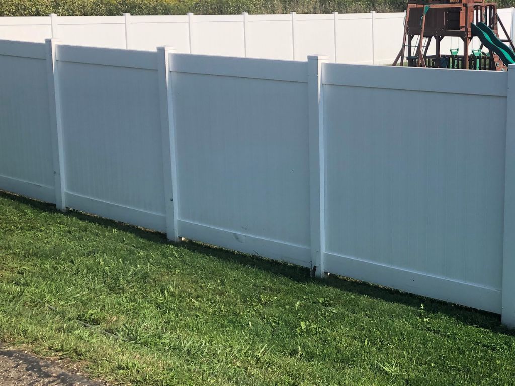 A white fence surrounds a playground in a backyard.