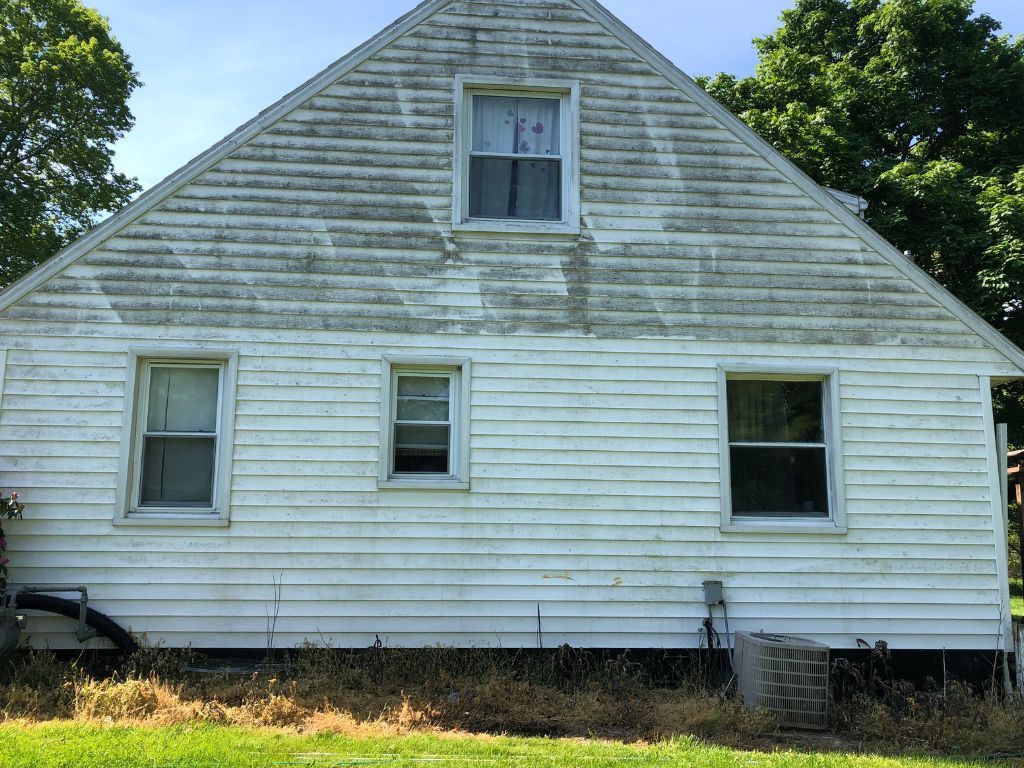 A white house with a triangle roof is sitting in the middle of a grassy field.