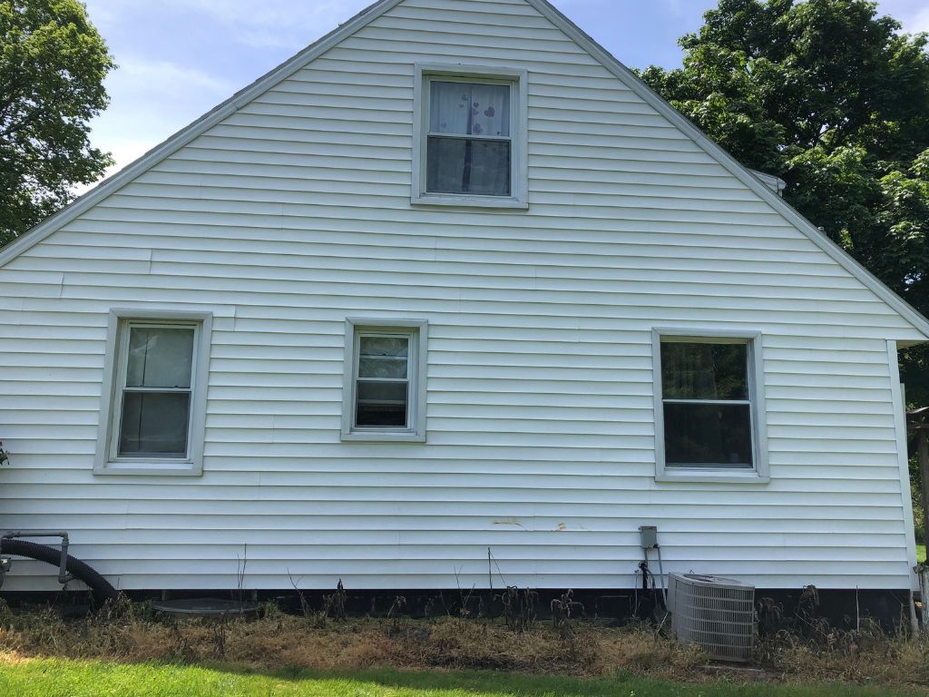 A white house with three windows is sitting on top of a lush green field.