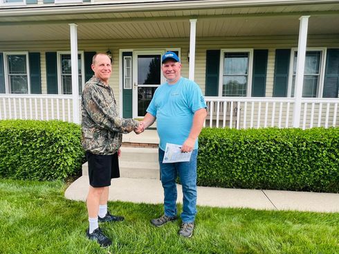 Two men are shaking hands in front of a house.