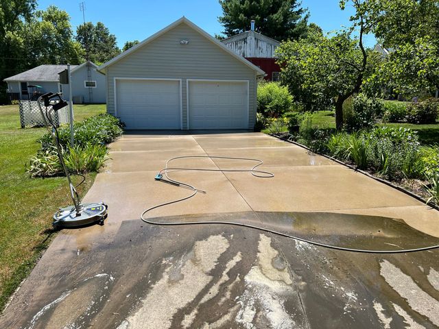 A driveway is being cleaned by a pressure washer in front of a garage.