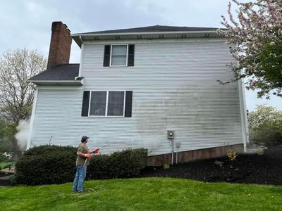 A man is cleaning the side of a white house with a pressure washer.