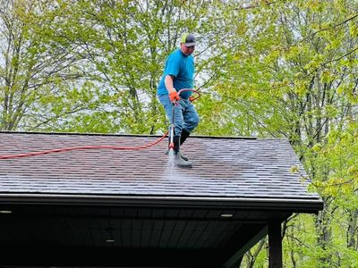 A man is cleaning the roof of a house with a pressure washer.