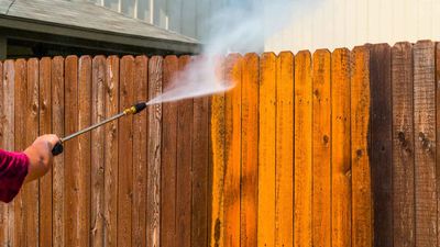 A person is cleaning a wooden fence with a high pressure washer.