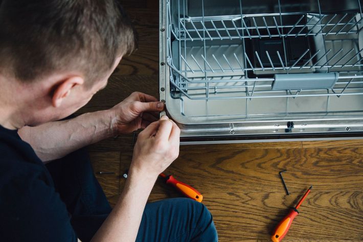 A man is fixing a washing machine in a kitchen.