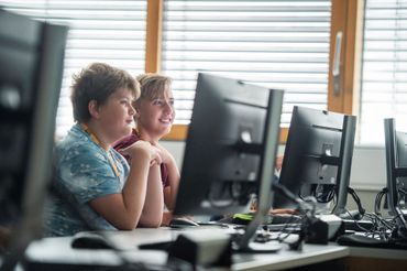 Zwei Kiner sitzen in einem Klassenzimmer vor Computerbildschirmen.