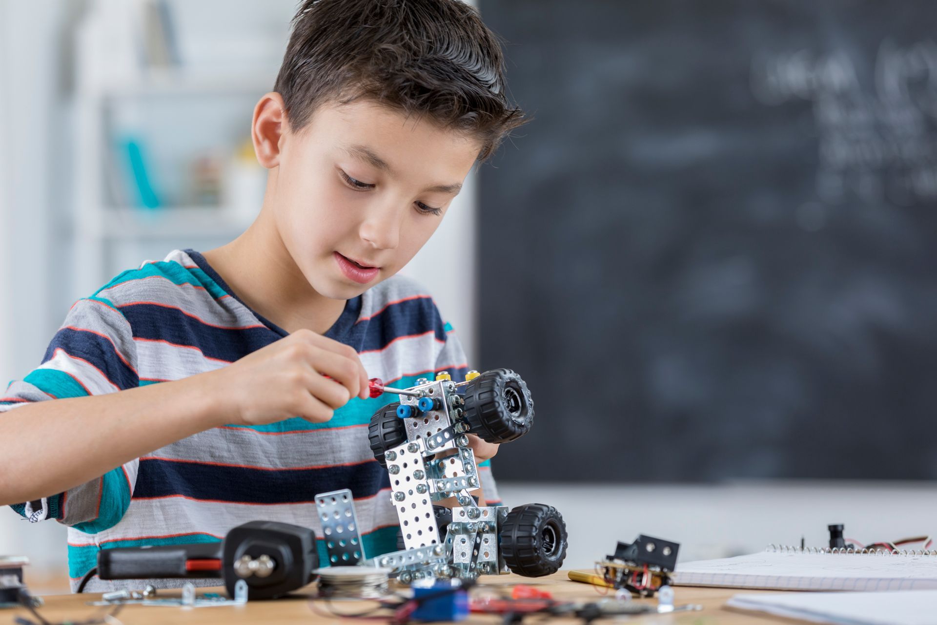 Ein kleiner Junge sitzt an einem Tisch und baut einen Roboter.