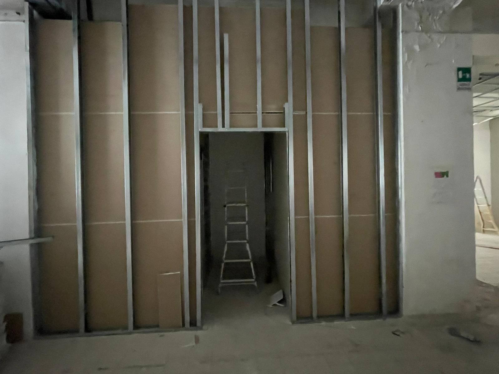 Costruzione interna: montanti metallici e cartongesso parzialmente installato che incorniciano la porta di un edificio.