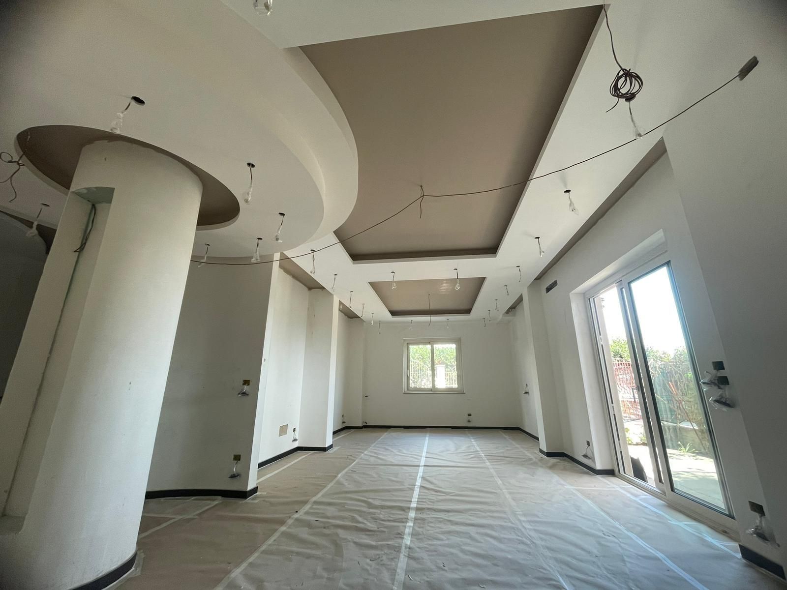 Stanza vuota in costruzione con pareti bianche e soffitto decorato. Rivestimento protettivo sul pavimento.