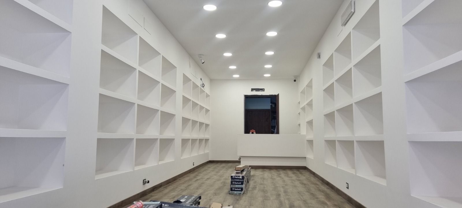 Una stanza bianca e vuota con scaffali incorporati su entrambi i lati, una finestra e luci dall'alto.