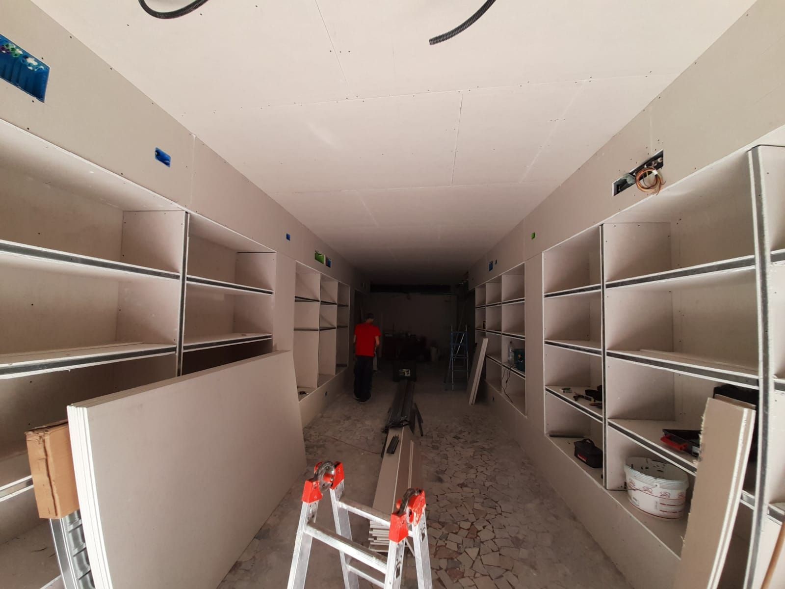 Sono in corso i lavori di ristrutturazione degli interni di una lunga stanza con scaffalature integrate e installazione di cartongesso.