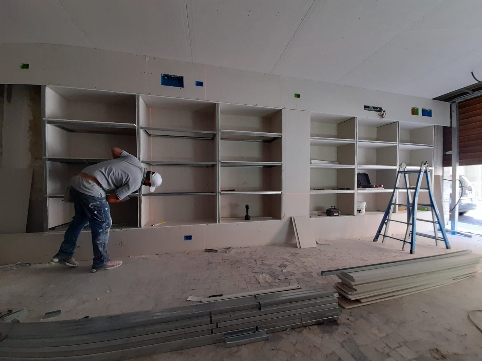 Operaio edile che installa cartongesso all'interno di una stanza con scaffali incorporati.
