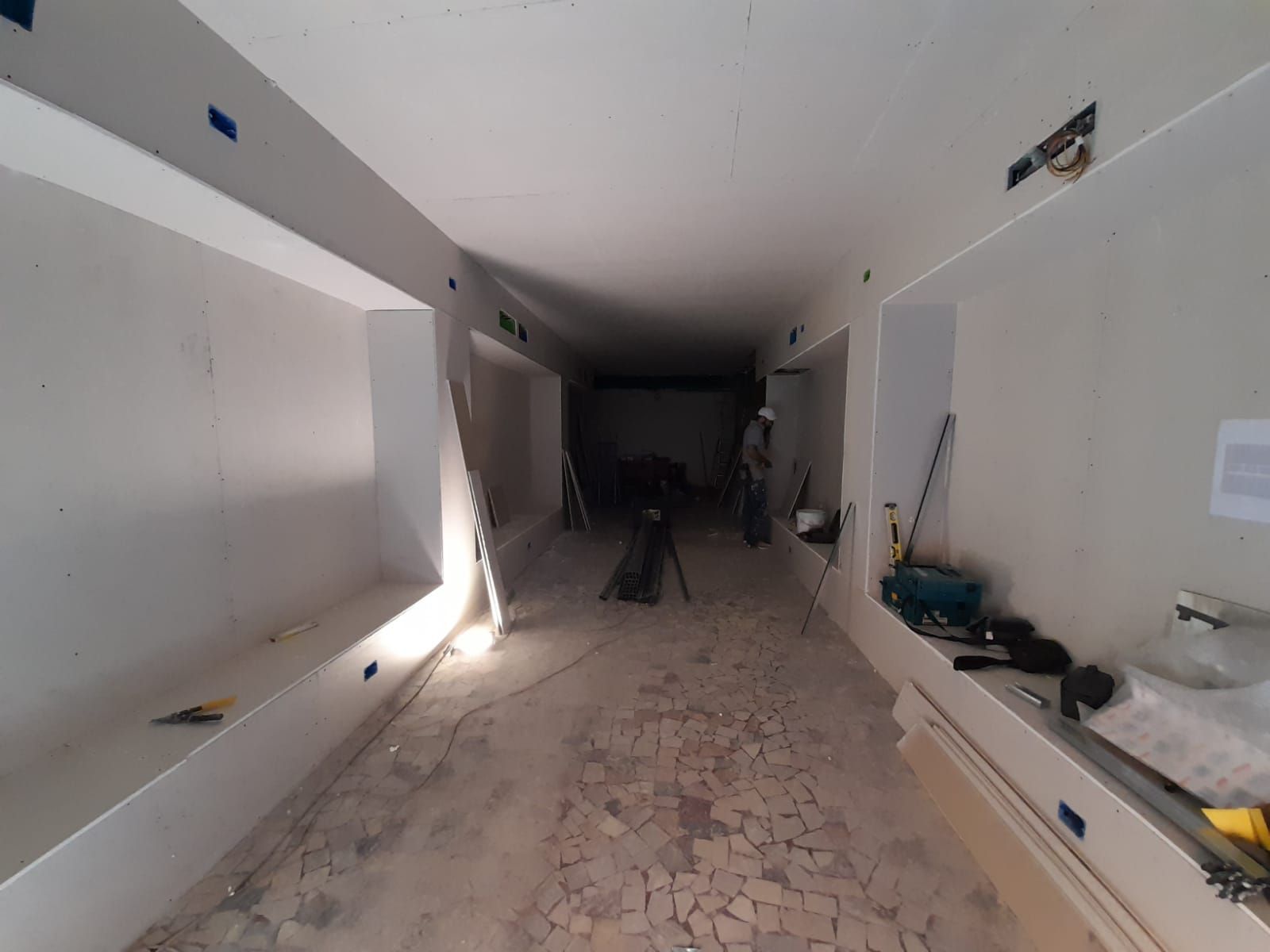 Cantiere interno con lungo corridoio, cartongesso, attrezzi e materiali da costruzione.