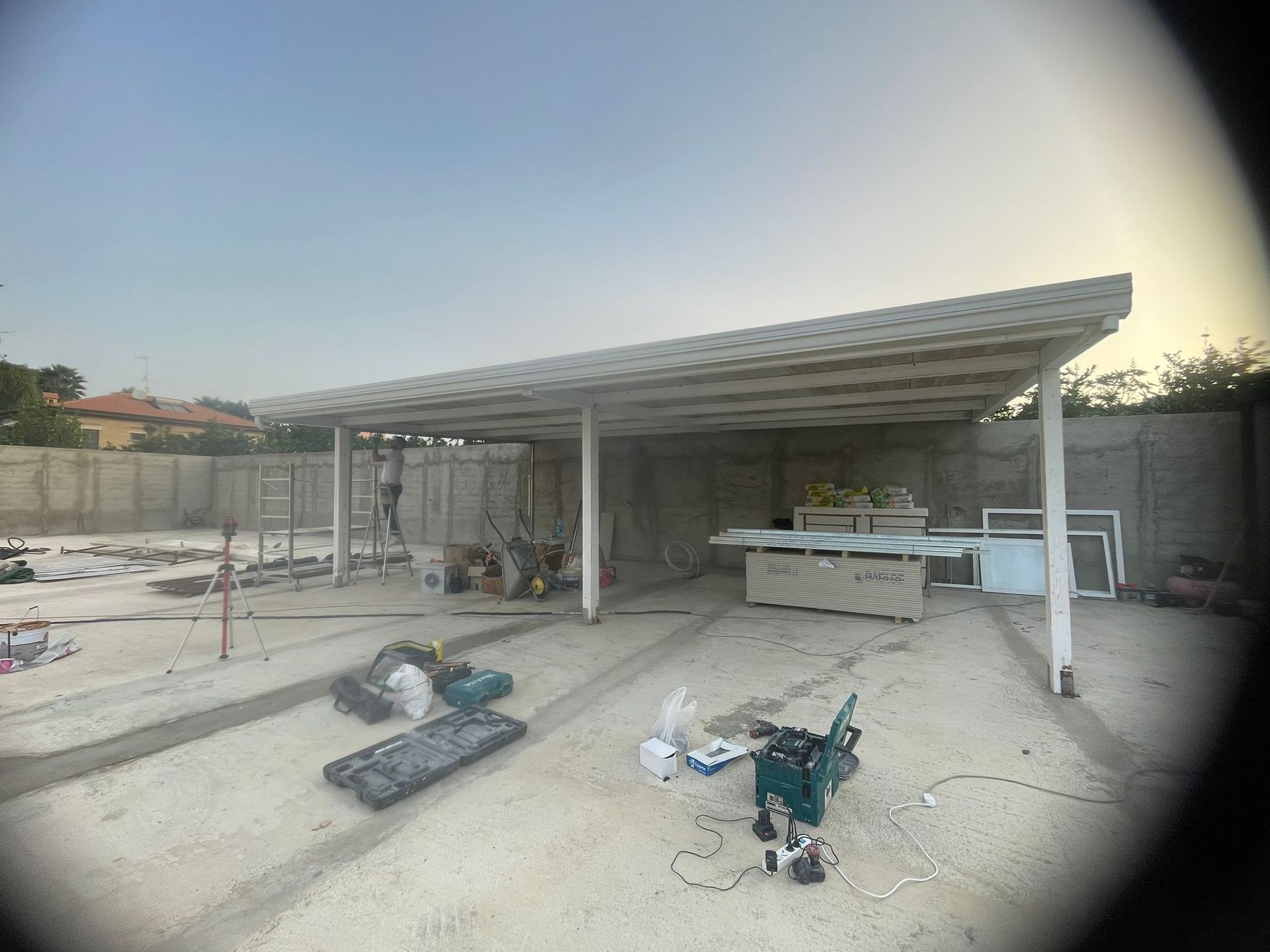 Cantiere con posto auto coperto bianco parzialmente realizzato e materiali da costruzione.