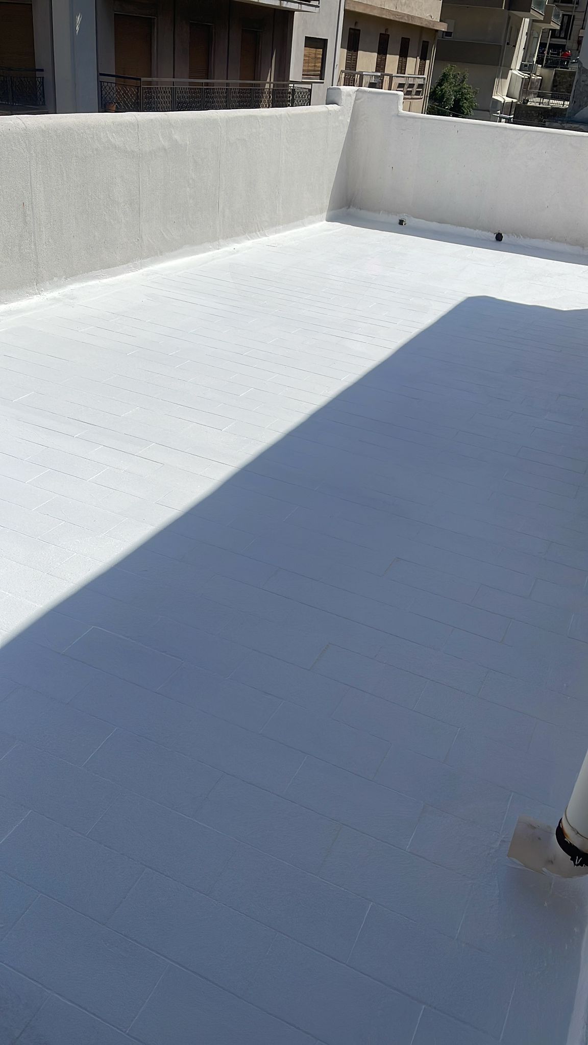 Tetto piatto dipinto di bianco con ombra parziale e pareti bianche circostanti.