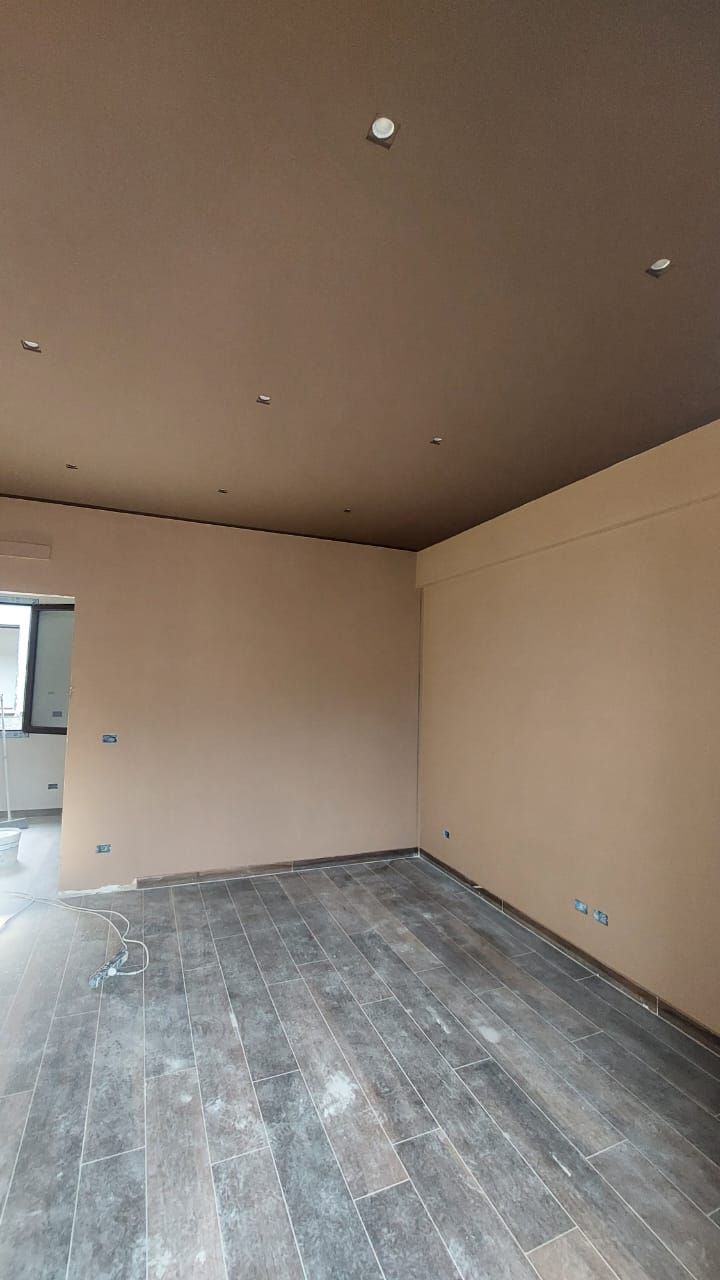 Stanza vuota con pavimenti in legno scuro, pareti marrone chiaro e un soffitto marrone più scuro con luci da incasso.