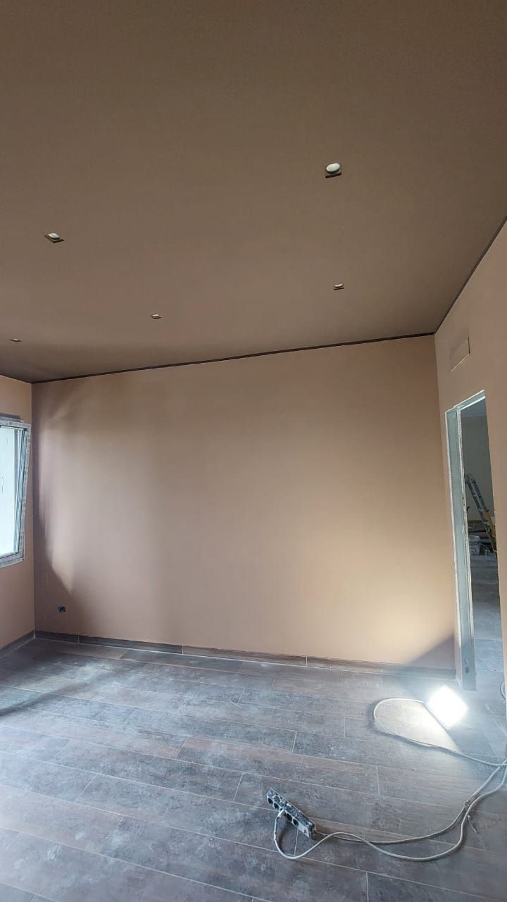 Una stanza con pareti e soffitto finiti, non tinteggiati; pavimento in cemento, porta a destra, finestra a sinistra.