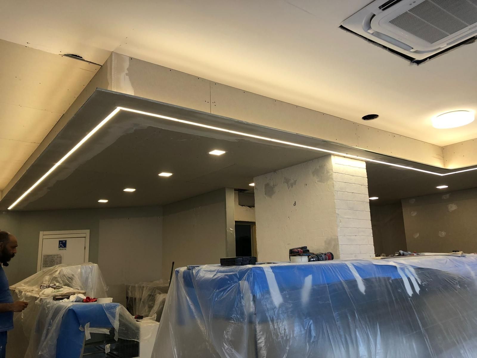 Interno in costruzione con illuminazione a incasso lungo il soffitto. Una persona è visibile sulla sinistra.