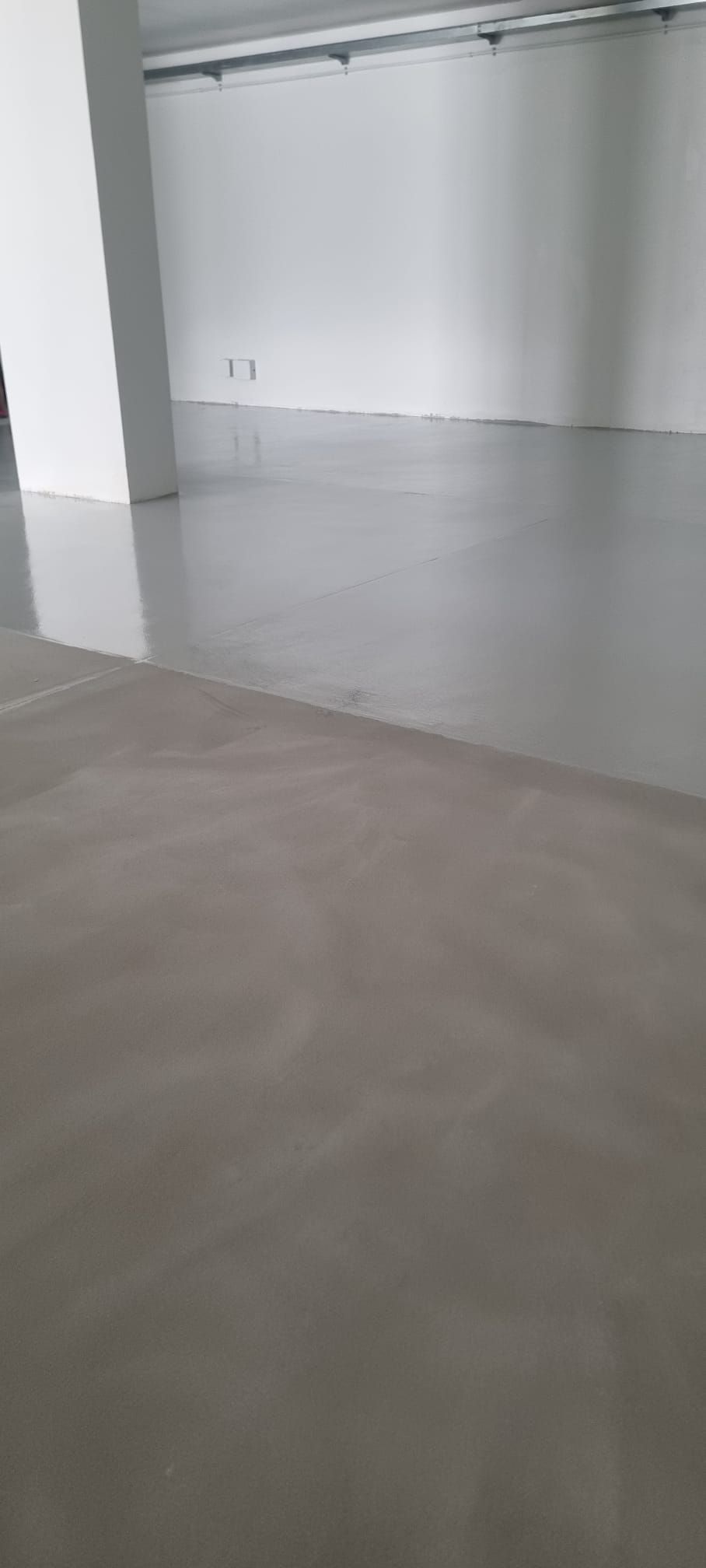 Vista interna di un edificio moderno con pavimento in cemento e pareti bianche.