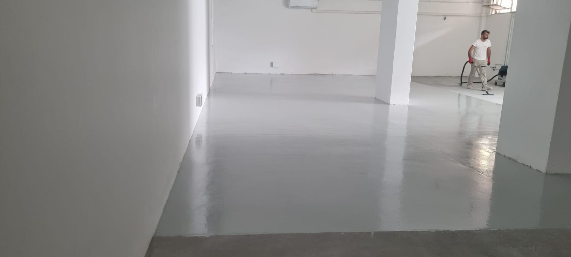 Una stanza vuota, appena dipinta, con un pavimento grigio lucido. Una persona sta lavorando sullo sfondo.