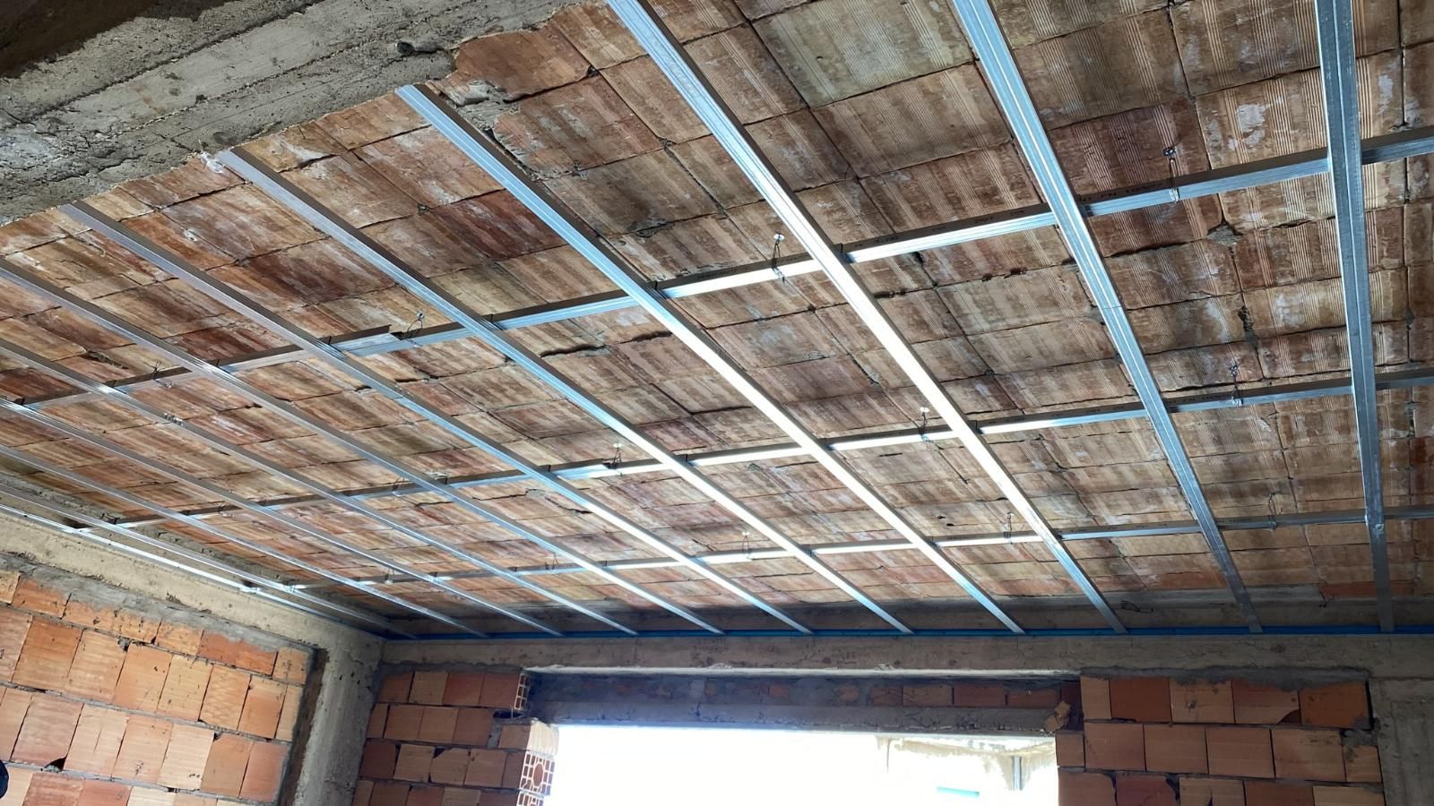 Soffitto in costruzione: mattoni a vista, griglia metallica, piastrelle rettangolari in una stanza.