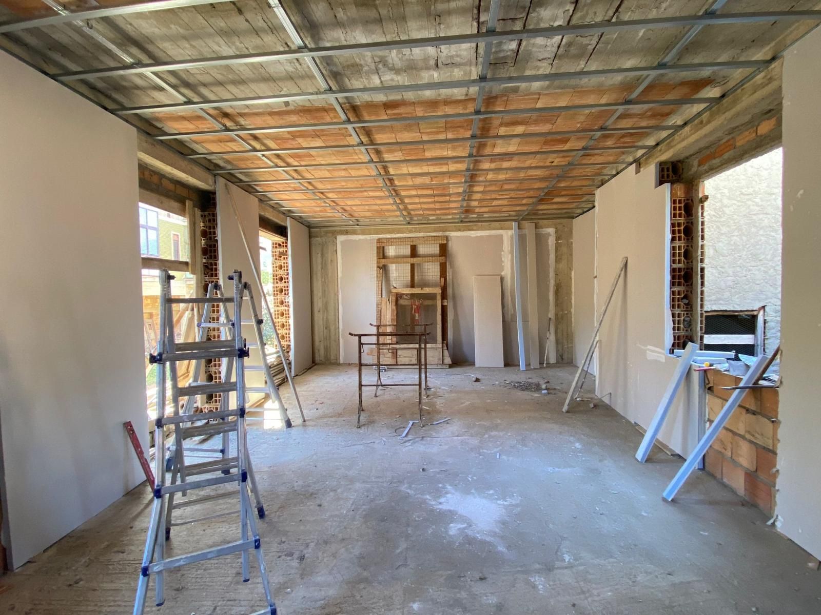 Stanza in fase di ristrutturazione con soffitto in mattoni a vista, cartongesso, scale e attrezzi.