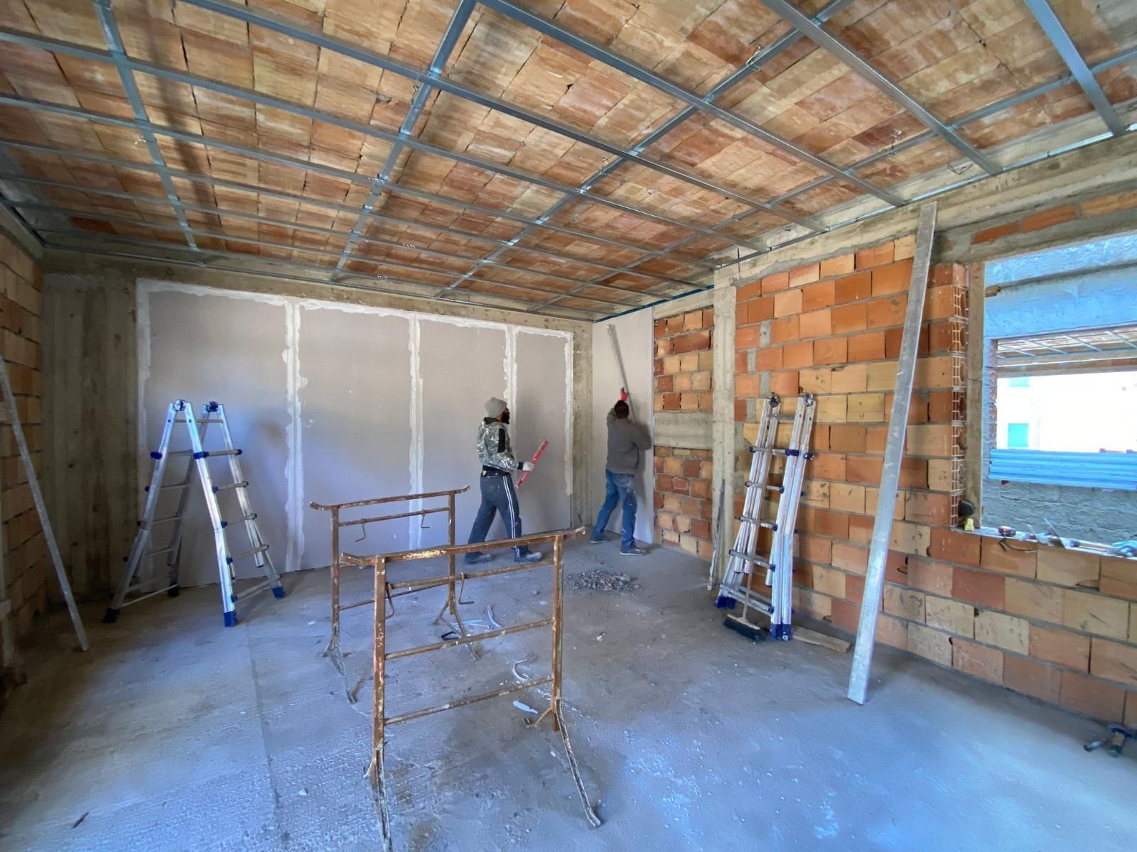 Cantiere: operai che installano cartongesso su una parete. Pareti in mattoni a vista, supporti metallici per il soffitto.