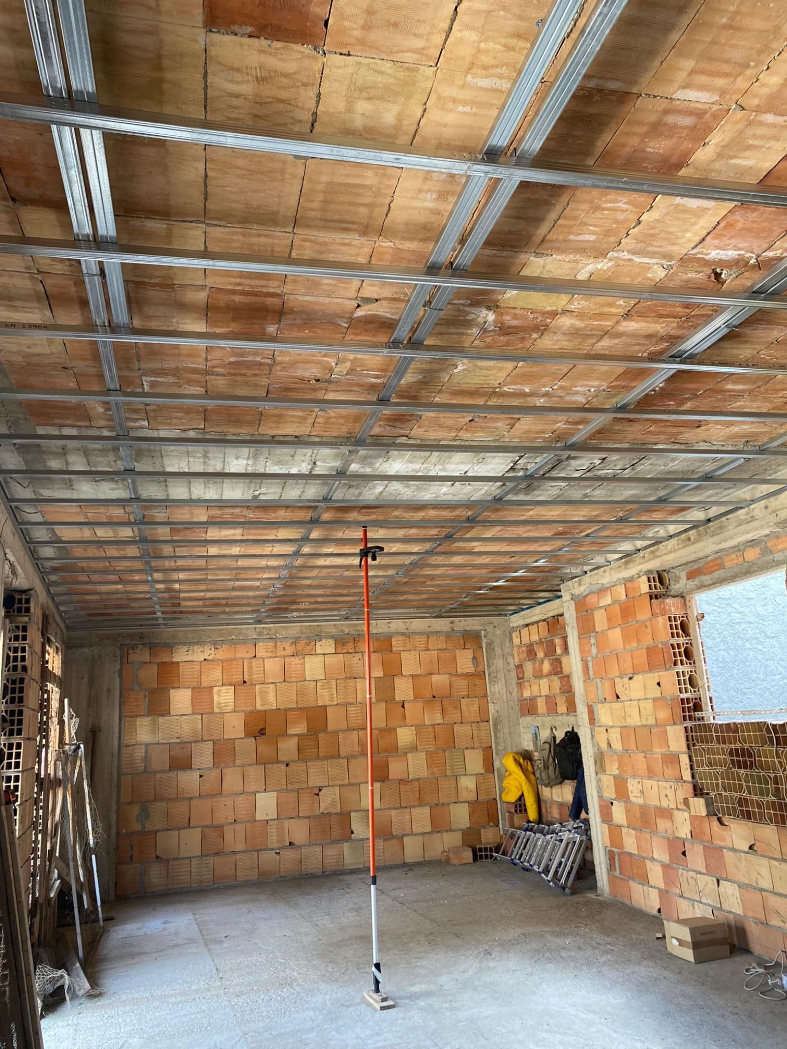 Interno di una stanza in costruzione con pareti in mattoni a vista, travi del soffitto e uno strumento di misurazione.